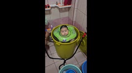 Baby with neck in inflatable ring floats in plastic bin full of water