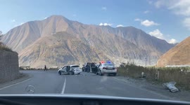 A traffic accident in the mountains of Georgia. A damaged vehicle is seen on the roadside, with police presence and emergency responders assessing the situation.