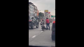 Motorcycle rider helps monitor lizard to cross a road in Thailand