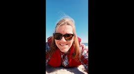 Smiling woman in sunglasses lies on sandy beach under blue sky. Enjoying sunny weather and ocean breeze in a casual, relaxing coastal moment of vacation