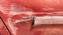 Close up video of a deep scratch and dent on a red car door caused by a collision, showing damaged paint, metal tear, and surface abrasions.