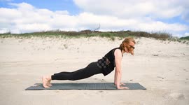 Woman practicing yoga outdoors on sandy surface, performing upward facing dog pose on mat, enjoying sunny weather, clear sky, and natural surroundings for relaxation and wellness