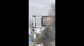 Thick smoke billowing up to 30 meters from a burning car on the M1 near Milton Keynes, causing major traffic disruption.