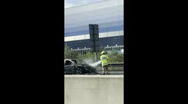 Firefighters extinguishing car fire on the M1 near Milton Keynes, with vehicle wreckage visible.