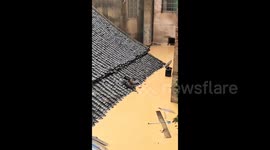 Elderly woman breaks through roof tiles and climbs to safety out of flooded home in China
