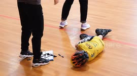 A young inline speed skating competitor lies on the ground after a fall during a tournament. A concerned coach or medic kneels beside, checking on the injured child inside a sports hall.