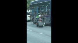 Tourist carries suitcase along road by dragging it behind motorcycle