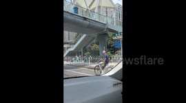 Elderly cyclist rides along balancing bottle of water on head