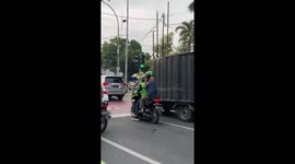 Elderly motorcycle passenger holds helmet instead of wearing it in Jakarta, Indonesia
