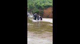 Men risk their lives carrying motorbikes through flash floods that are pouring into their village