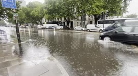 Vehicles drive through flooded London roads.