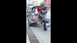Rider sits on the back of tuktuk while dragging broken scooter