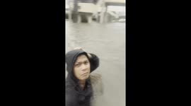 Local wades through flood to reach SUV submerged in water