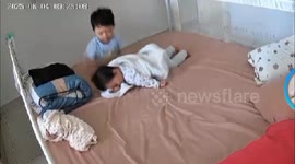Big brother watches over baby sister in bed while mom tidies up in Kuala Lumpur, Malaysia