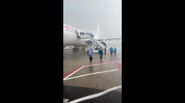 Passengers wearing raincoats run to plane during storm