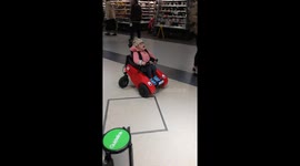 Whizzy Wheelchair Fun: Adorable Girl's Spirited Spin While Waiting. Cute little girl in a red wheelchair spins it around and around whilst waiting for her mum in a queue