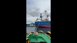 Three tugboats drag giant cargo ship out of port