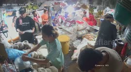 Market vendor falls over while standing on bucket to hang stock