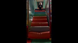 Little boy extends his legs and launches himself down a padded ramp