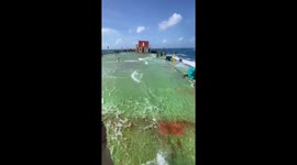 Seafarers enjoy themselves on the deck as waves crash over them on the ship