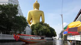 Tourists enjoy feeding fish from a boat while admiring massive golden Buddha statue