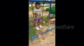 A cute 3 year old girl having fun on a swing in a playground.