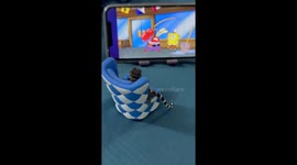 Gecko watches cartoon while sitting in miniature armchair