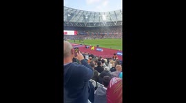 Woman in yellow raincoat rests beside football field in West Ham, England
