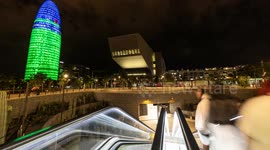 Night time timelpase of the glories park and metro station with the torre agbar skyscraper lit up at night in barcelona, spain