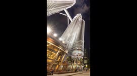 The petronas twin towers in kuala Lumpur lit up at night with crowds of people on the streets below