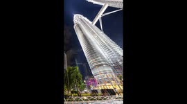 The petronas twin towers in kuala Lumpur lit up at night with crowds of people on the streets below