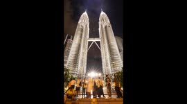 The petronas twin towers in kuala Lumpur lit up at night with crowds of people on the streets below