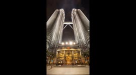 The petronas twin towers in kuala Lumpur lit up at night with crowds of people on the streets below