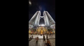 The petronas twin towers in kuala Lumpur lit up at night with crowds of people on the streets below