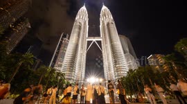 The petronas twin towers in kuala Lumpur lit up at night with crowds of people on the streets below