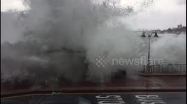 Massive waves crash against sea wall and spill onto promenade