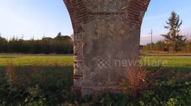 Aerial shot, foggy fields, an ancient roman aqueduct and cars driving behind it, filmed with drone