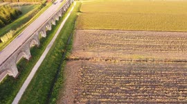 Aerial shot, foggy fields, an ancient roman aqueduct and cars driving behind it, filmed with drone