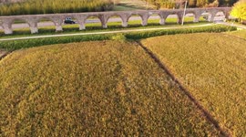 Aerial shot, foggy fields, an ancient roman aqueduct and cars driving behind it, filmed with drone