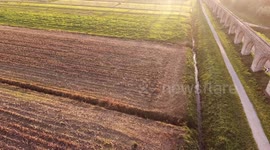 Aerial shot, foggy fields, an ancient roman aqueduct and cars driving behind it, filmed with drone