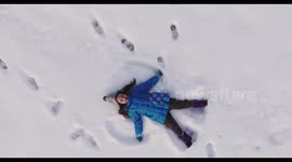 Aerial shot of a little girl making a snow angel in the snow, 4K