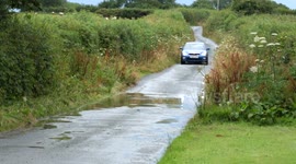 Car drivers through flood causing huge spray on both sides.