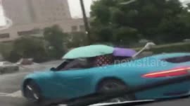 Convertible passengers use umbrellas to protect themselves from the rain