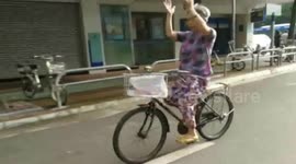 Elderly woman claps her hands in the air while riding a bike