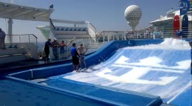 Young man falls whilst attempting to surf on Flowrider surf simulator onboard cruise ship