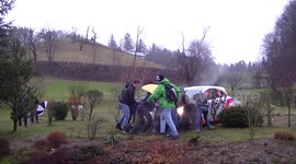 Rally spectators push a car out of a muddy garden after crash