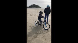Child learning to ride a bike on the beach in Marazion, Cornwall with the family