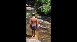 Epic summer family fun:  Daddy leads the way knee sliding into natural pools at waterfall before being followed by his excited and eager children .