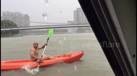Bare-chested man paddles canoe along swelling river