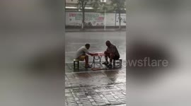 Men play chess calmly in heavy rain